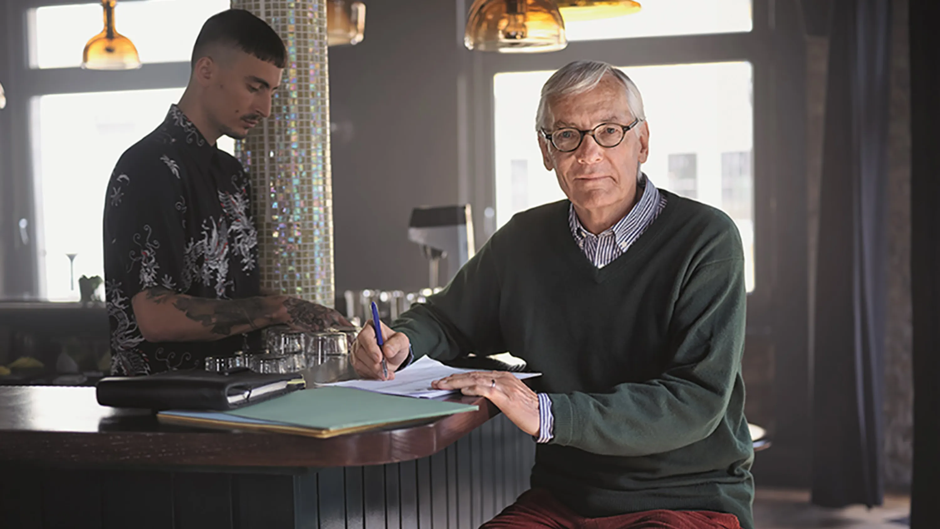 Ein älterer Mann sitzt in einem Café an der Bar und prüft Dokumente