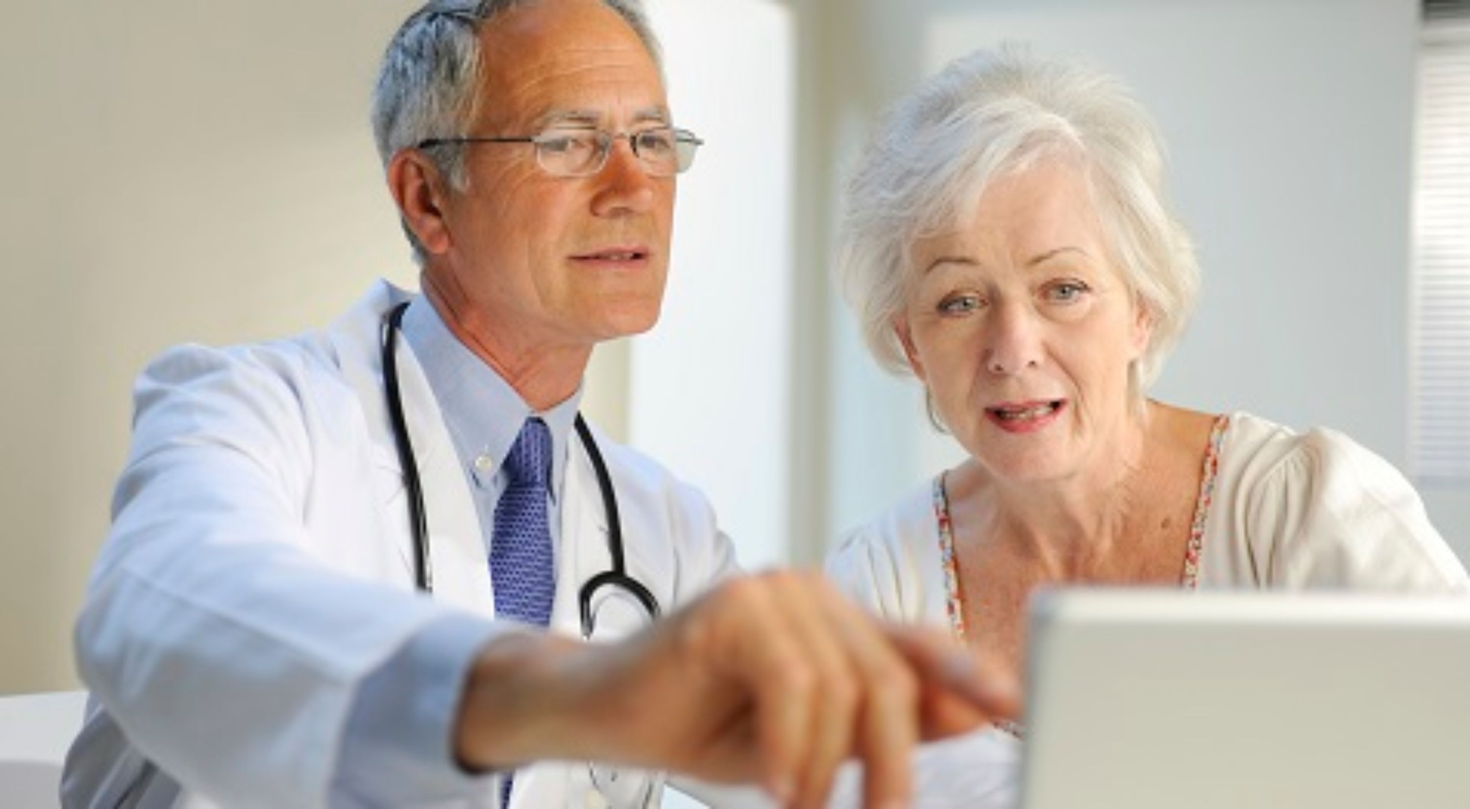 Ein Arzt und eine ältere Patientin vor dem Laptop.