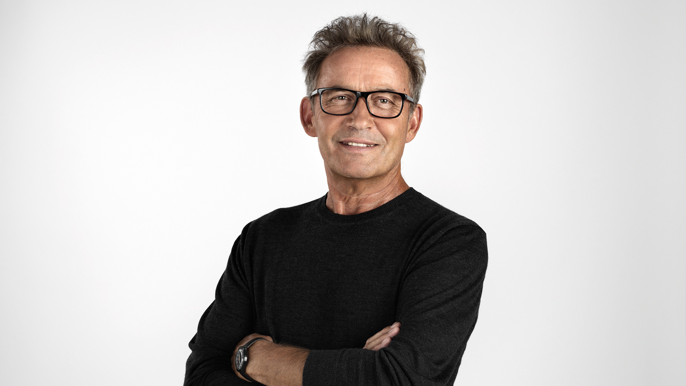 Älterer Mann mit verschränkten Armen und Brille, der lächelt.